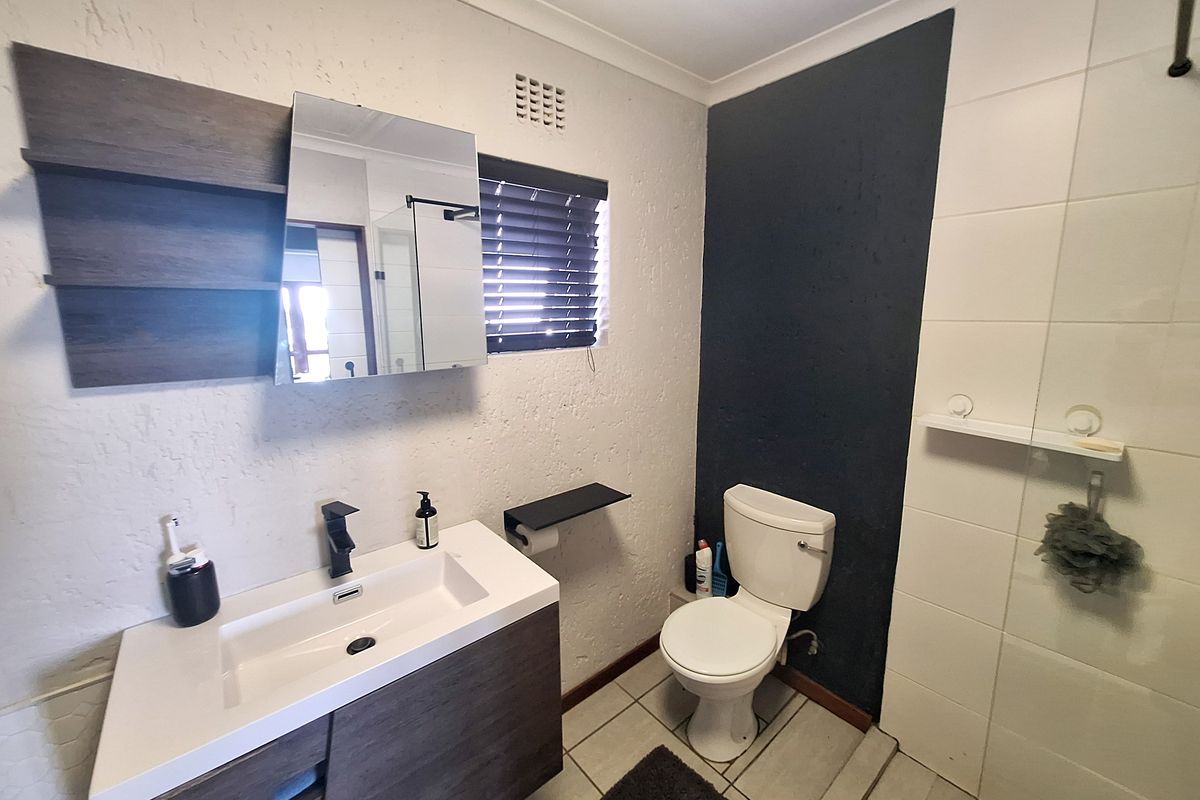 Modern bathroom featuring a vanity with basin, toilet, and a glass-enclosed shower with tiled finishes.