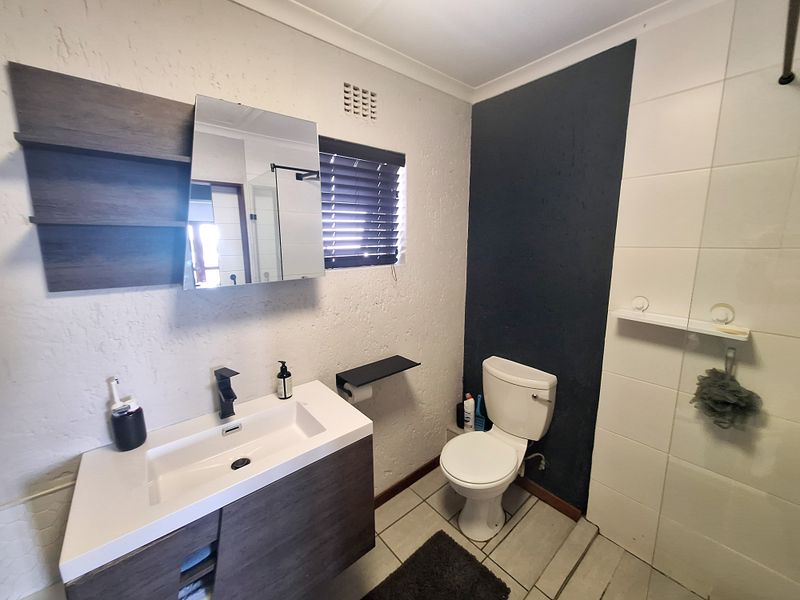 Modern bathroom featuring a vanity with basin, toilet, and a glass-enclosed shower with tiled finishes.