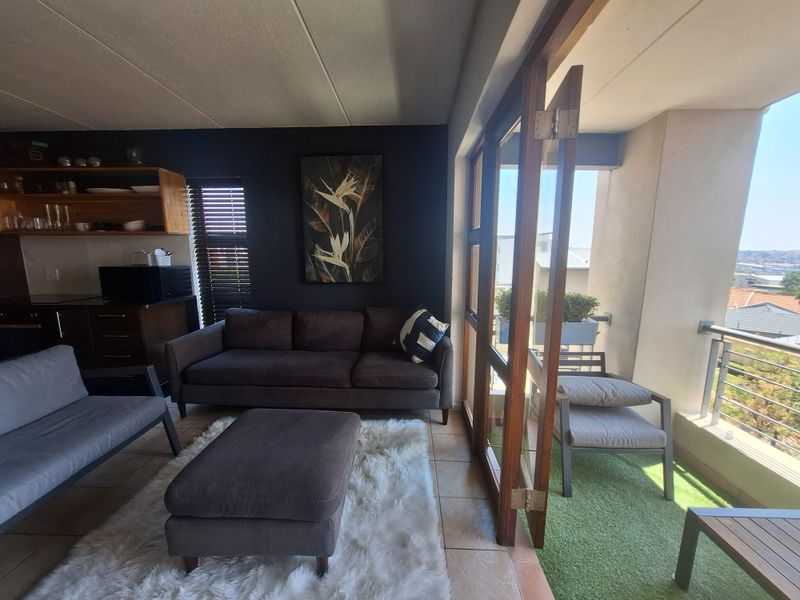 Open-plan living area featuring tiled floors and timber-framed glass doors leading to a private balcony with outdoor views.