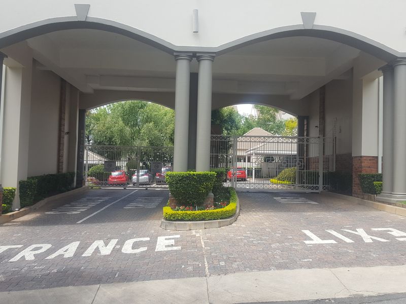 A secure gated entrance to the apartment complex featuring a paved driveway, decorative columns, and a well-maintained facade.