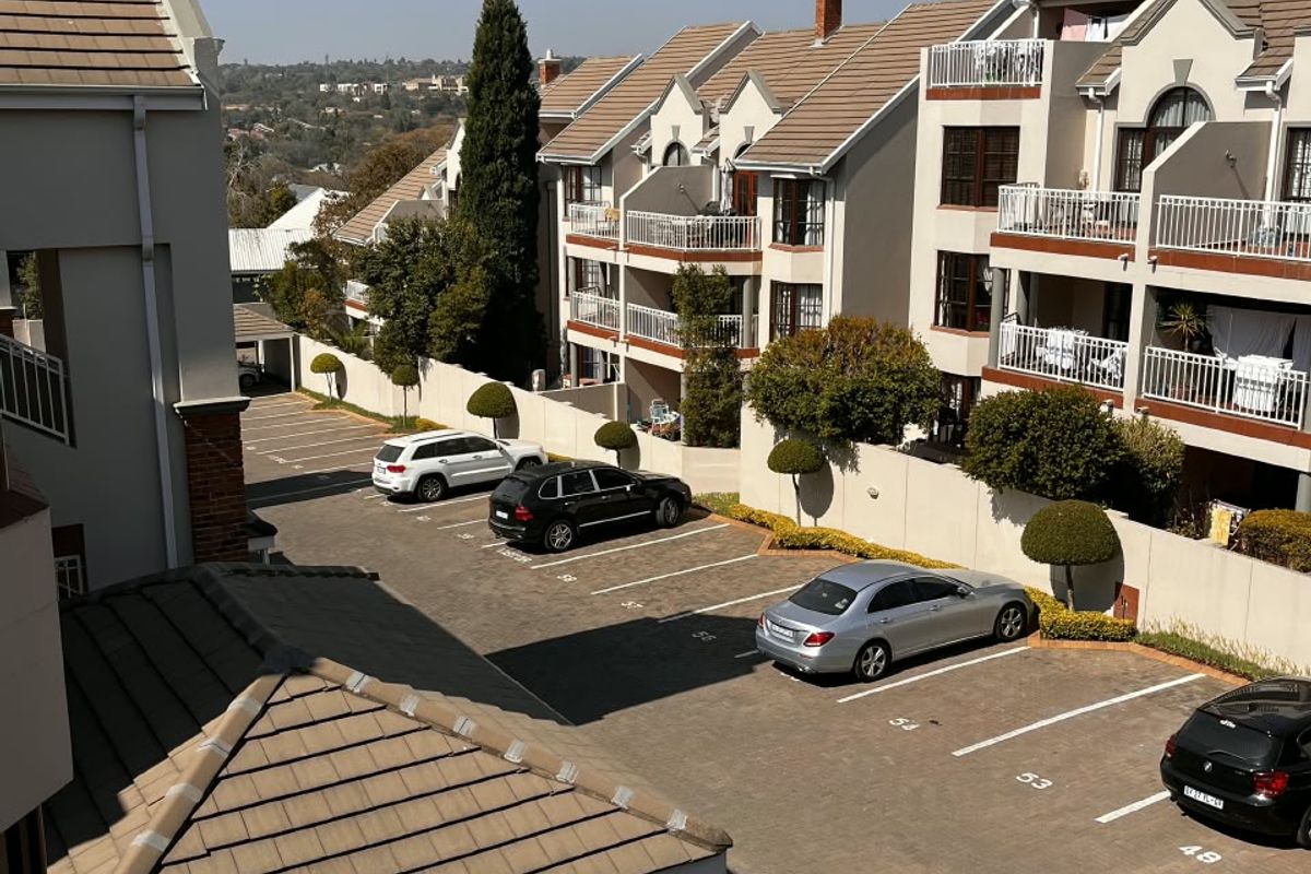 An elevated view of the apartment complex exterior, featuring paved parking bays, carports, and multi-story residential units with balconies.
