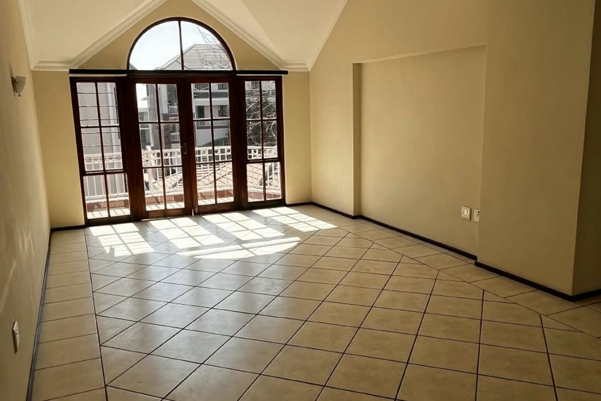 Spacious living area featuring vaulted ceilings, ceramic tile flooring, and large arched windows with access to a balcony.