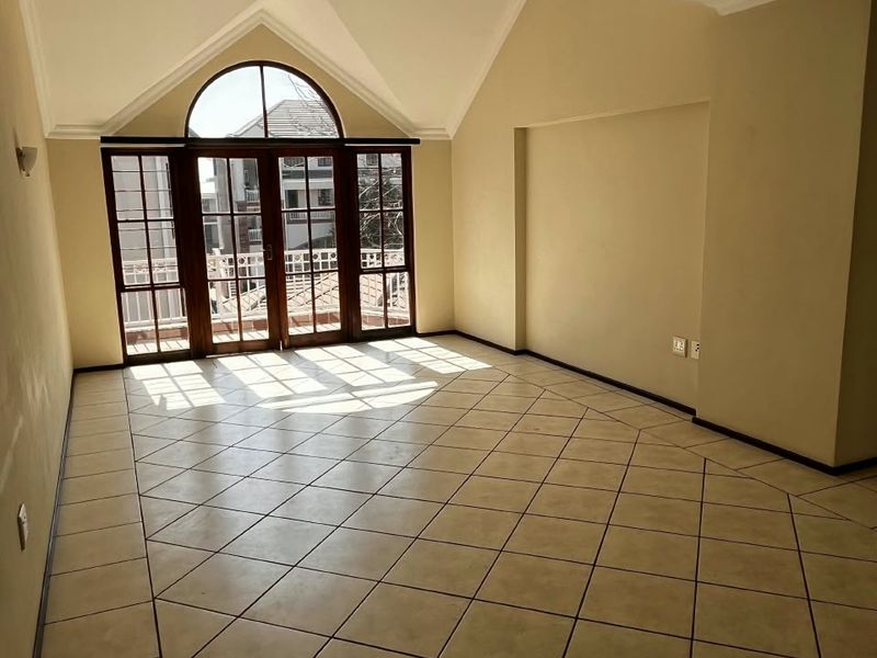 Spacious living area featuring vaulted ceilings, ceramic tile flooring, and large arched windows with access to a balcony.