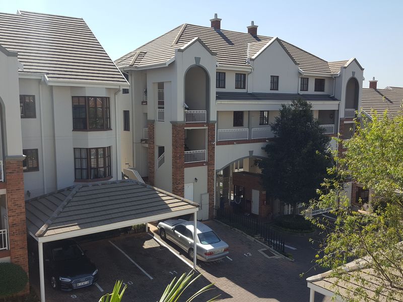 An elevated view of a multi-story apartment complex featuring brick and plaster facades, tiled roofing, private balconies, and a covered carport area.