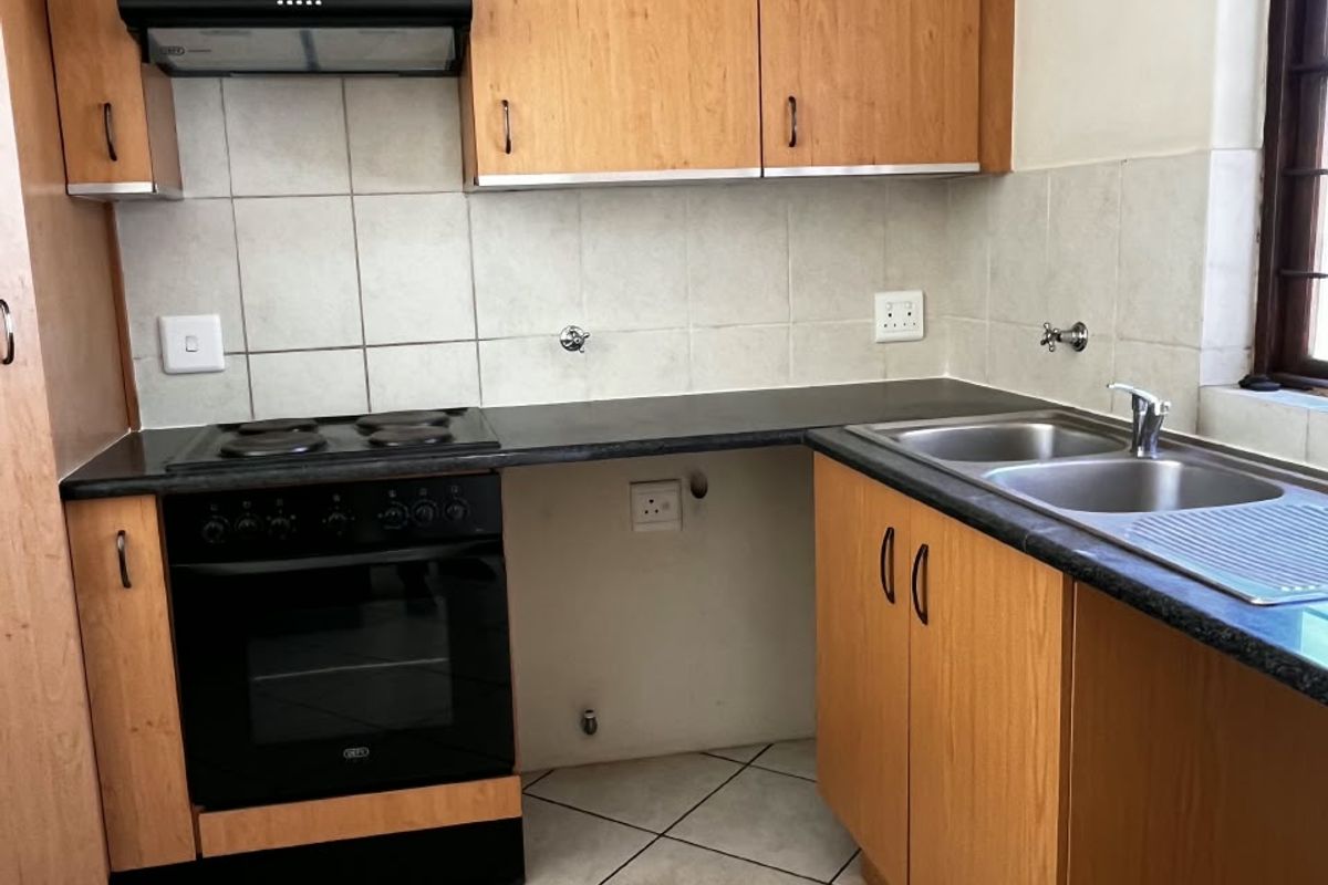 A functional kitchen featuring laminate cabinetry, a built-in oven with hob, extractor fan, and a double bowl stainless steel sink with tiled splashback.