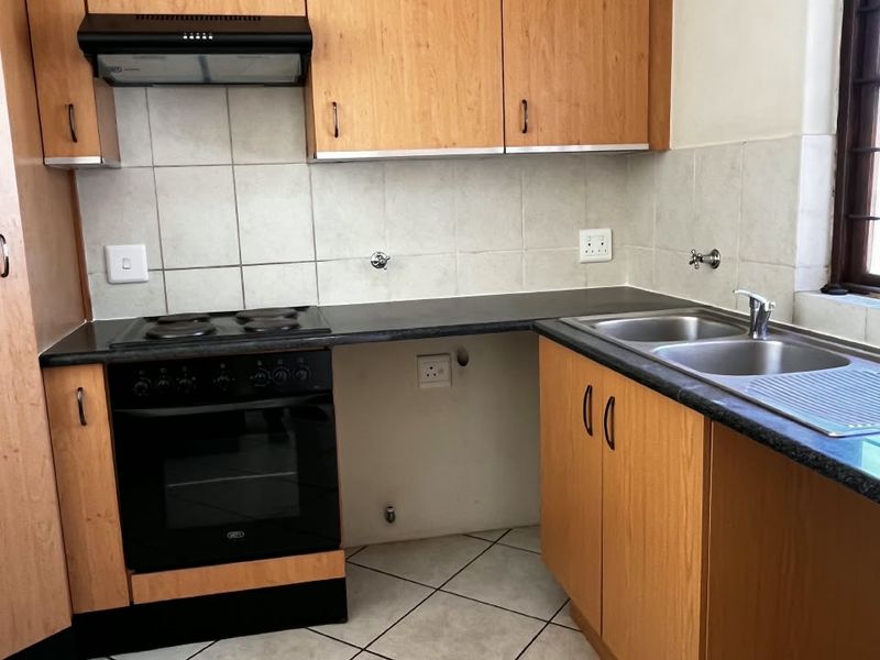 A functional kitchen featuring laminate cabinetry, a built-in oven with hob, extractor fan, and a double bowl stainless steel sink with tiled splashback.