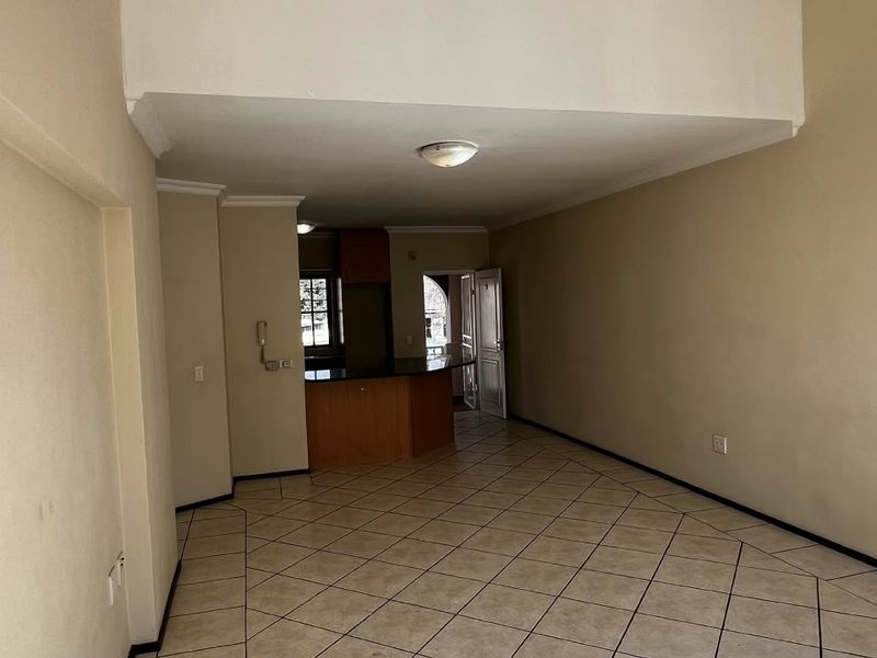 Spacious open-plan living area featuring tiled flooring, a breakfast bar, and built-in kitchen cabinetry, offering a versatile layout for modern apartment living.