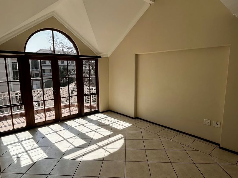 Spacious living area featuring a high vaulted ceiling, large arched window, and glass french doors leading to a balcony, finished with ceramic tile flooring.