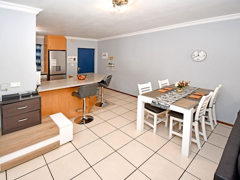 Open-plan living and dining area featuring ceramic floor tiles, a breakfast bar with granite countertop, and neutral wall finishes.