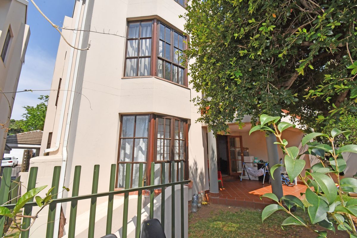 Rear view of the apartment building featuring a tiled patio area, bay windows, and metal security fencing.
