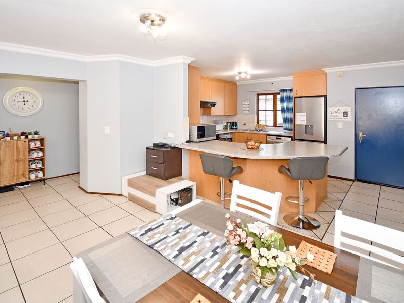Open-plan kitchen and dining area featuring light wood cabinetry, laminate countertops, a breakfast bar, and neutral ceramic floor tiles throughout.