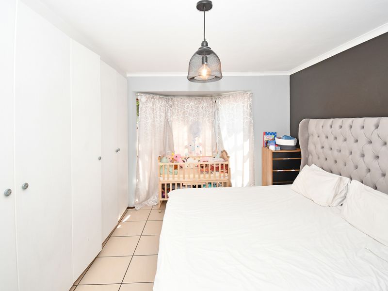 A well-maintained bedroom featuring built-in cupboards, tiled flooring, and a modern pendant light fixture, offering a clean and functional living space.
