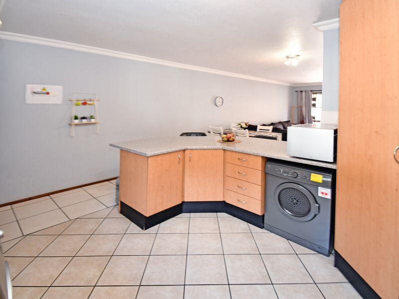 Open-plan kitchen and living area featuring light wood cabinetry, granite-look countertops, tiled flooring, and an integrated washing machine.