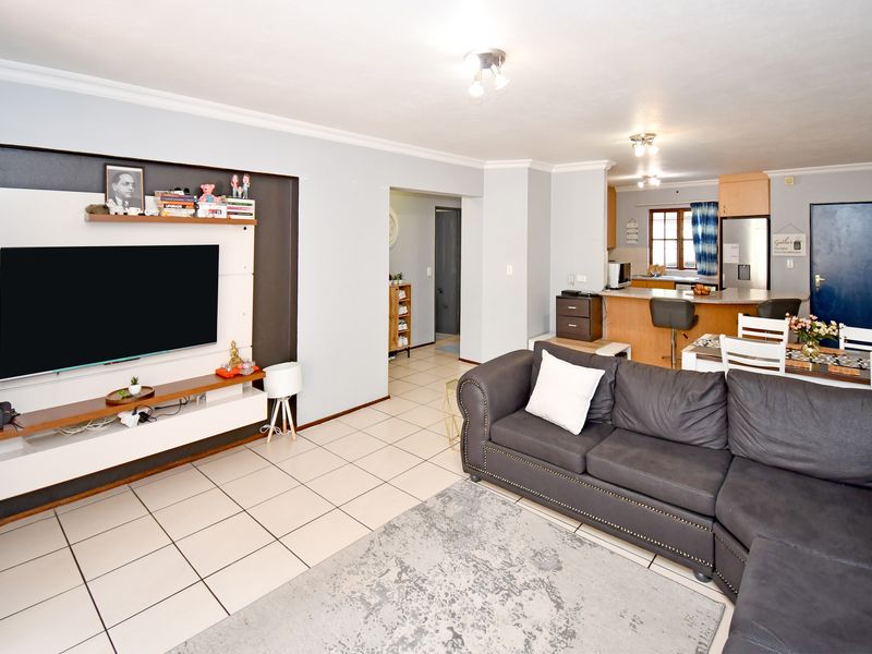 Open-plan living and kitchen area featuring tiled flooring, a built-in media wall, and a functional kitchen with a breakfast island.