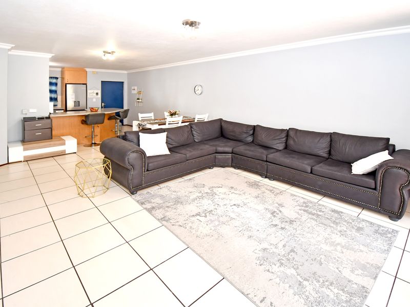 Spacious open-plan living area featuring tiled flooring, a functional kitchen with island seating, and a comfortable lounge space.