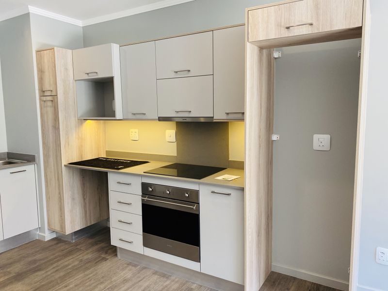 Modern kitchen featuring light wood-tone and matte grey cabinetry, integrated oven and hob, stone countertops, and under-cabinet lighting in a clean, contemporary finish.