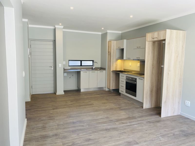 Modern open-plan kitchen featuring light wood-tone cabinetry, integrated oven and hob, and durable laminate flooring in a clean, neutral-toned living space.