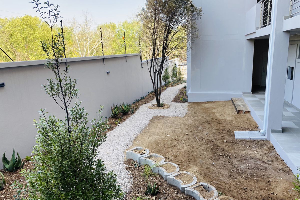 A rear garden area featuring a gravel pathway, perimeter wall with electric fencing, and an adjacent tiled patio space awaiting final landscaping.