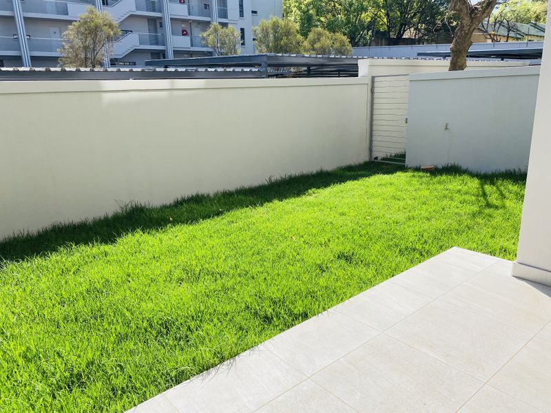 A private garden area featuring a well-maintained lawn, a tiled patio space, and a secure perimeter wall with a pedestrian gate.