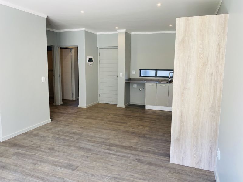 A bright and modern open-plan living area featuring neutral walls, durable laminate flooring, recessed lighting, and a compact, functional kitchen corner.