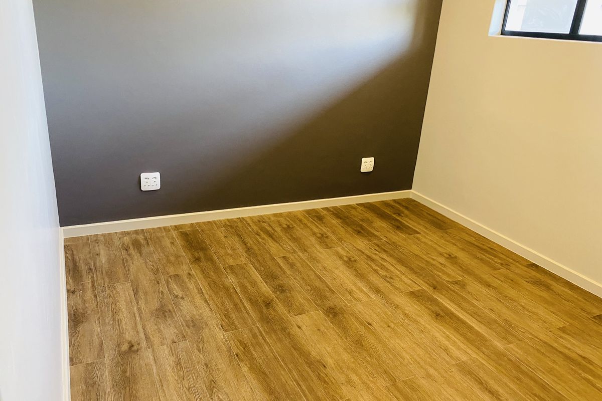A clean, empty bedroom featuring modern laminate wood flooring, a dark accent wall, and a window with a black frame.