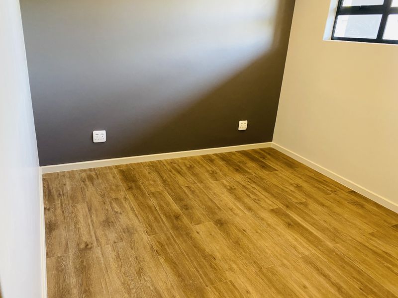 A clean, empty bedroom featuring modern laminate wood flooring, a dark accent wall, and a window with a black frame.