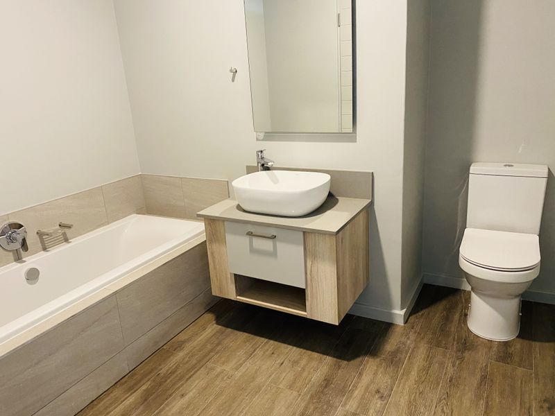 A modern, clean bathroom featuring a built-in bathtub, a contemporary wall-mounted vanity with a vessel sink, and a separate toilet.