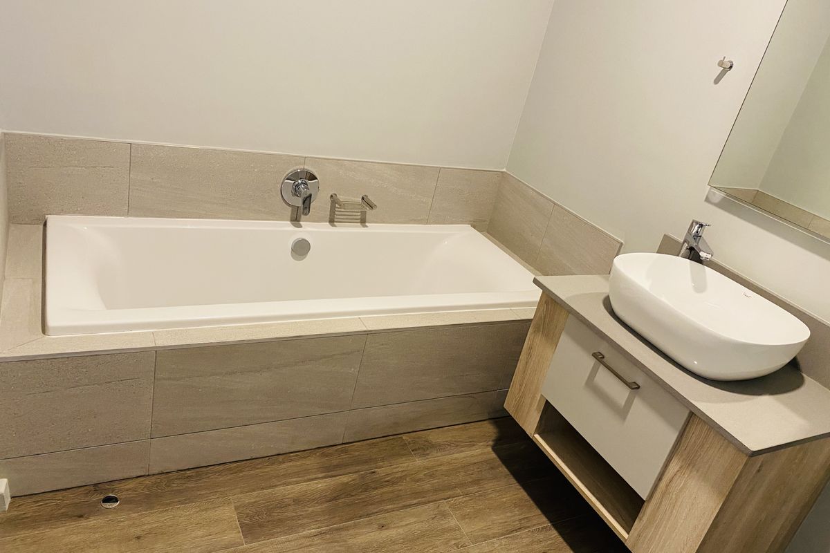Modern bathroom featuring a built-in bathtub with tiled surround, a contemporary vanity with a vessel sink, and wood-look flooring.