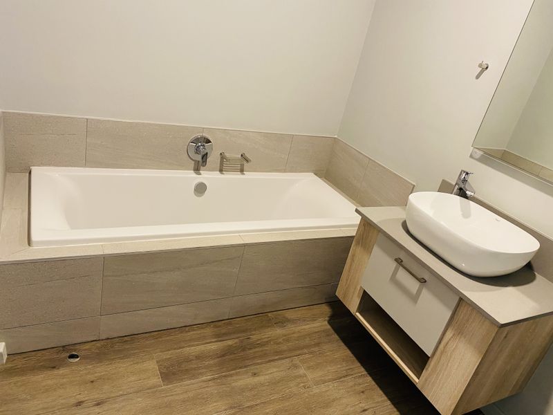 Modern bathroom featuring a built-in bathtub with tiled surround, a contemporary vanity with a vessel sink, and wood-look flooring.