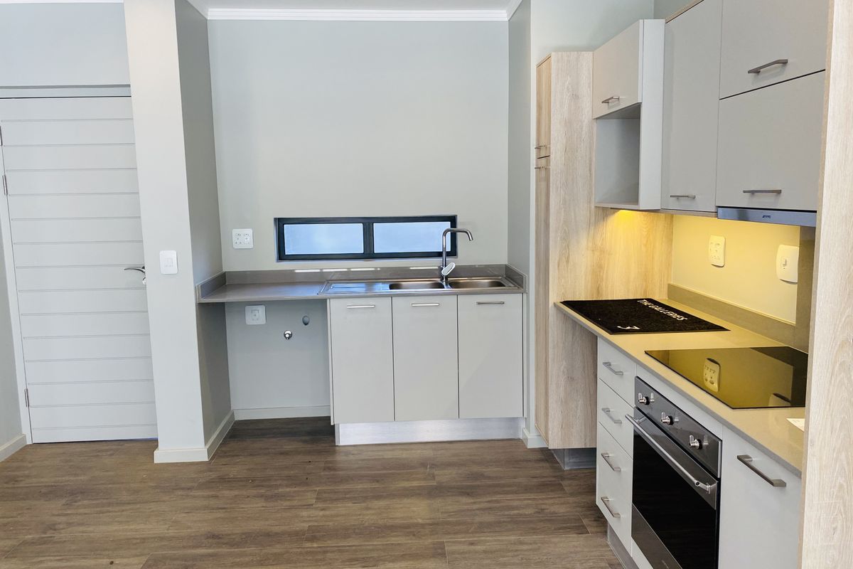 Modern kitchen featuring sleek cabinetry, stone countertops, integrated electric hob and oven, and high-quality laminate flooring in a clean, contemporary layout.