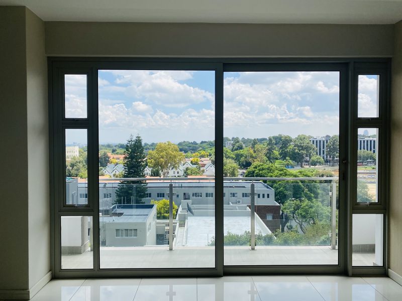 A bright, empty room featuring large sliding glass doors that open onto a balcony with a clear view of the surrounding neighbourhood.