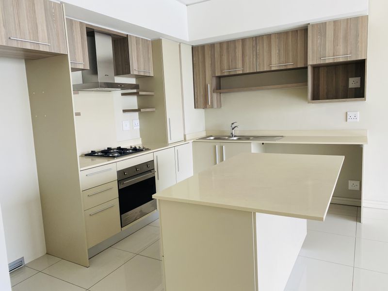 Modern kitchen featuring light-toned cabinetry, stone countertops, a central island, and integrated stainless steel appliances including a gas hob and oven.