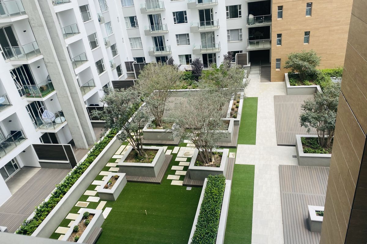 An elevated view of a modern apartment complex courtyard featuring landscaped gardens, raised planter boxes, synthetic lawn areas, and timber decking.