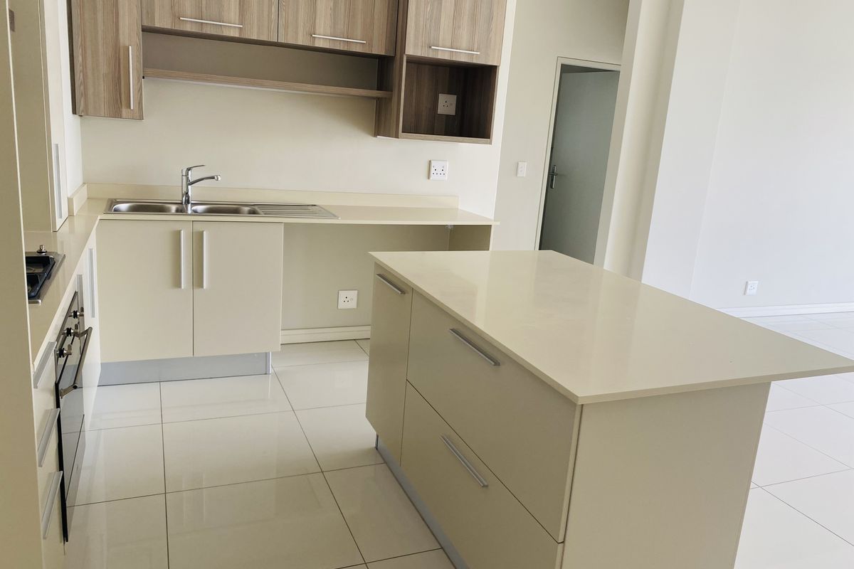 Modern kitchen featuring light-toned cabinetry, stone countertops, a central island, and integrated appliances with clean tiled flooring.