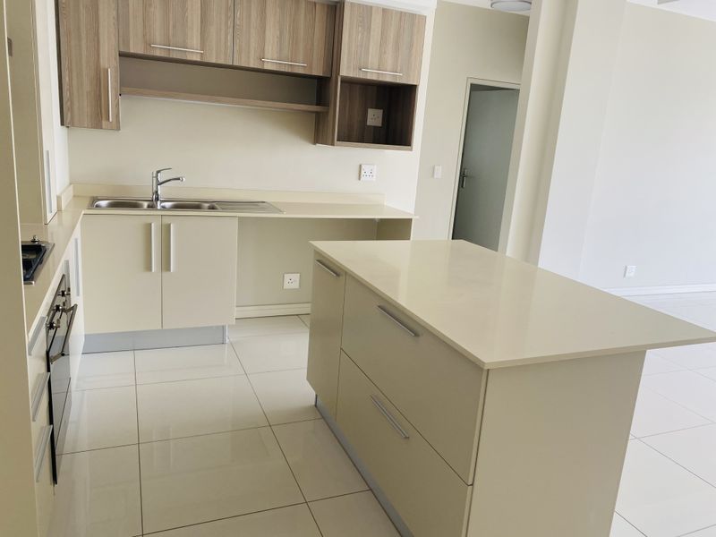 Modern kitchen featuring light-toned cabinetry, stone countertops, a central island, and integrated appliances with clean tiled flooring.