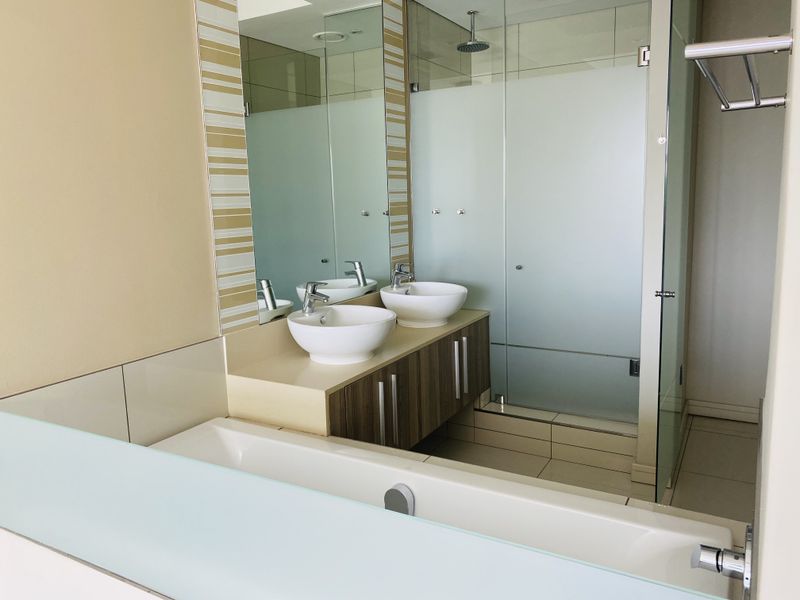 Modern bathroom featuring a double vanity with vessel sinks, wall-mounted faucets, and a spacious walk-in shower with a glass enclosure.