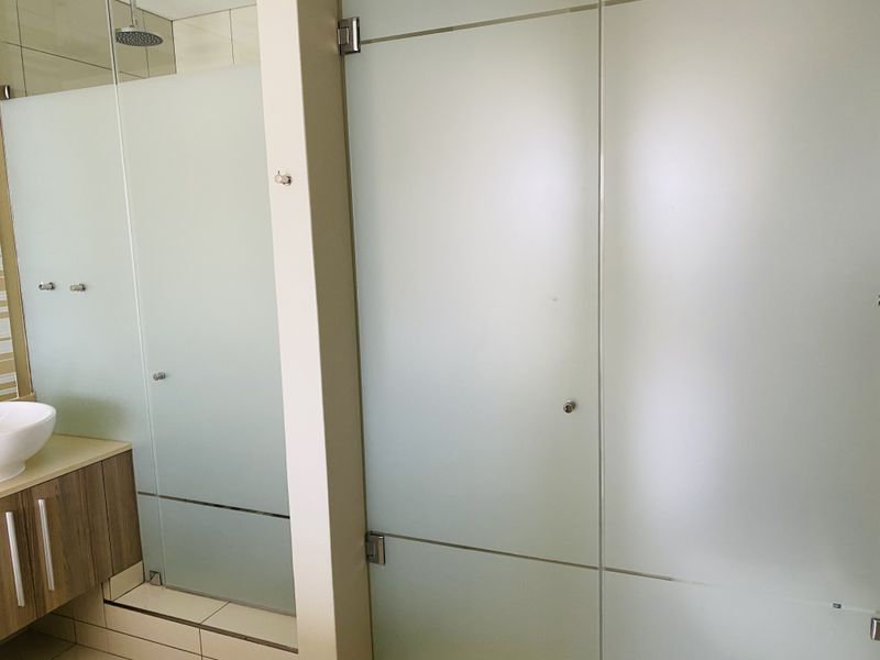 Modern bathroom featuring a vanity with a countertop basin and a spacious walk-in shower enclosed by frosted glass panels.