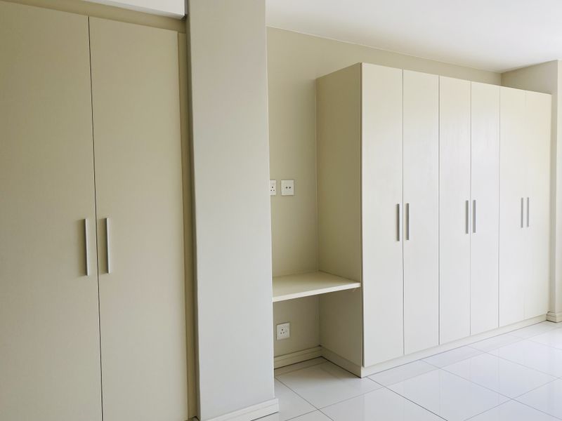 A bright bedroom featuring extensive built-in cabinetry with an integrated desk area and clean, modern tiled flooring.