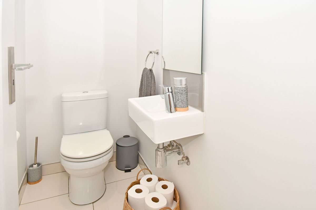 A compact guest bathroom featuring a modern wall-mounted basin, chrome fixtures, and a standard toilet with tiled flooring.