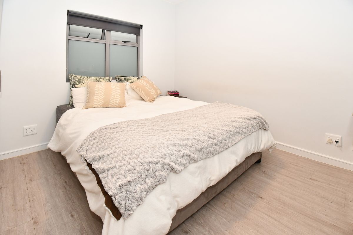 A clean and well-maintained bedroom featuring light-toned laminate flooring, neutral walls, and an aluminium-framed window with a fitted roller blind.