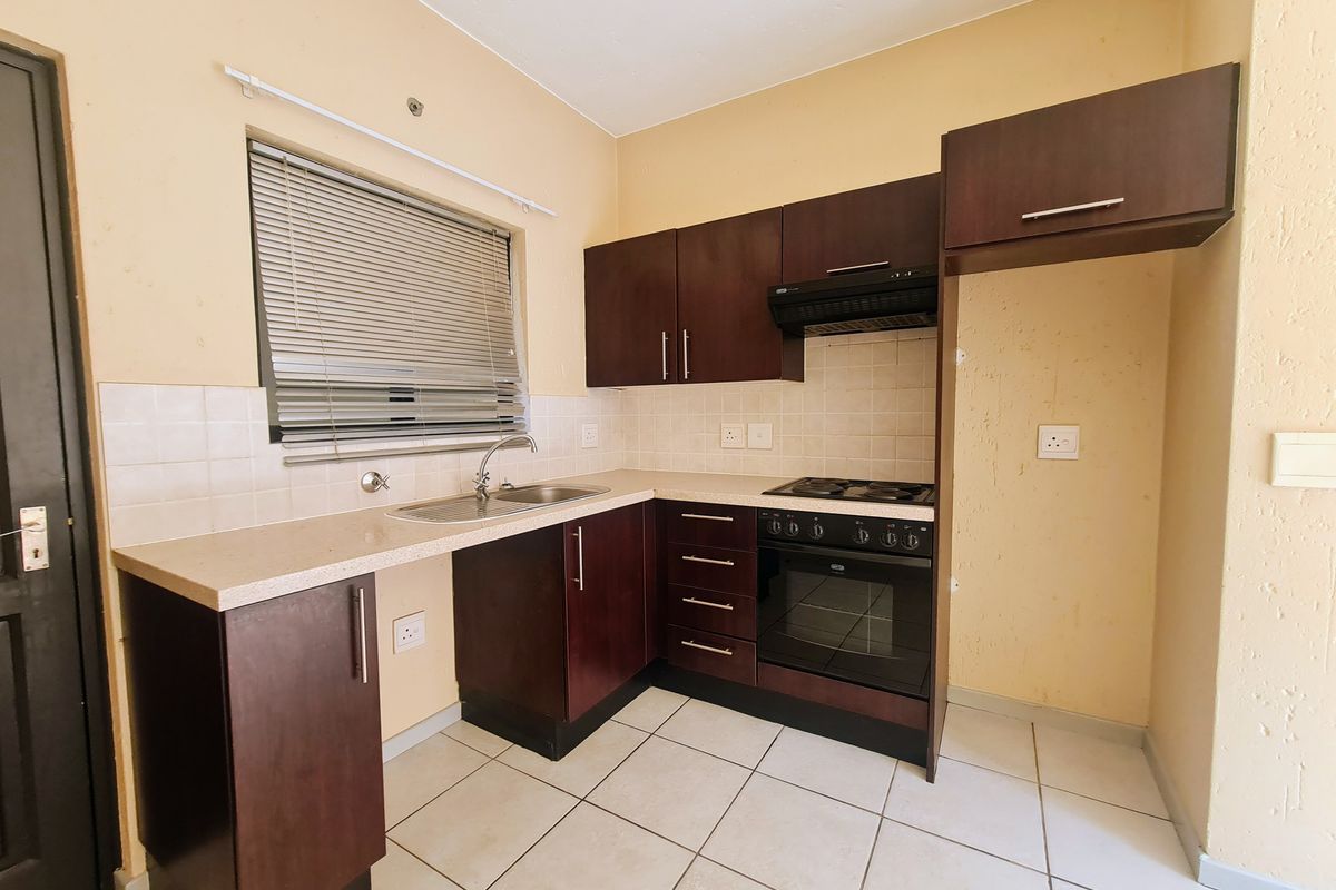 A functional kitchen featuring dark wood cabinetry, built-in oven with hob, extractor fan, and tiled flooring, offering a clean and practical workspace.
