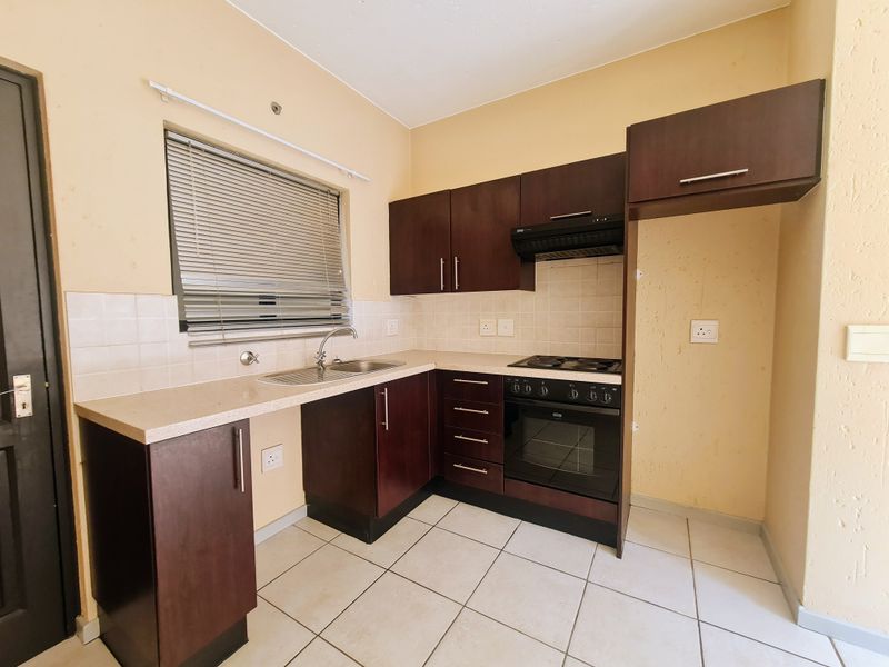 A functional kitchen featuring dark wood cabinetry, built-in oven with hob, extractor fan, and tiled flooring, offering a clean and practical workspace.