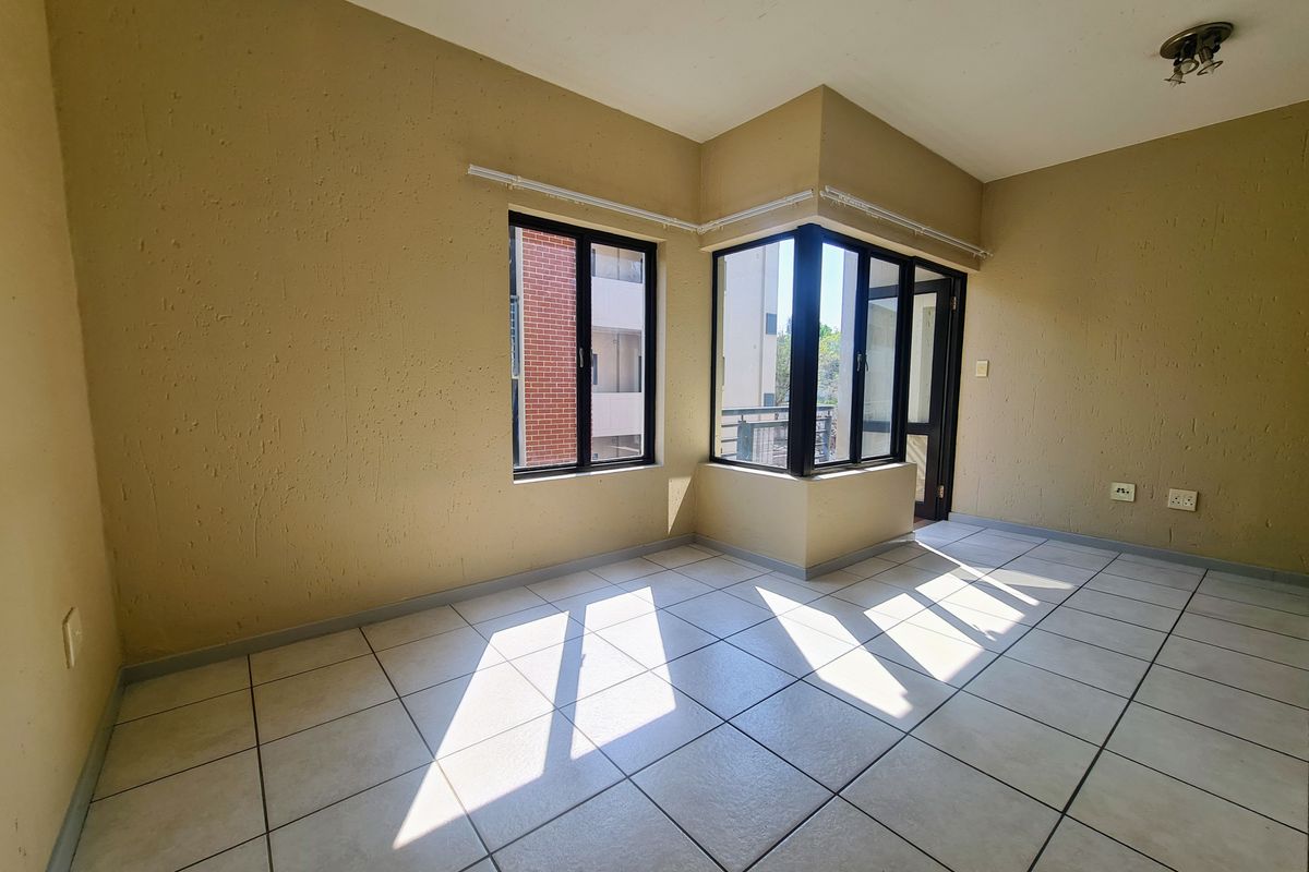 An empty living area featuring tiled flooring, textured walls, and corner windows that provide natural light and access to an outdoor space.