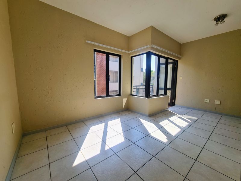 An empty living area featuring tiled flooring, textured walls, and corner windows that provide natural light and access to an outdoor space.