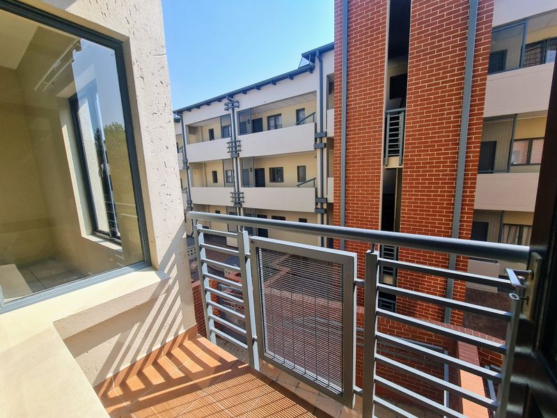 A private balcony featuring tiled flooring and a secure metal balustrade, overlooking the apartment complex courtyard.