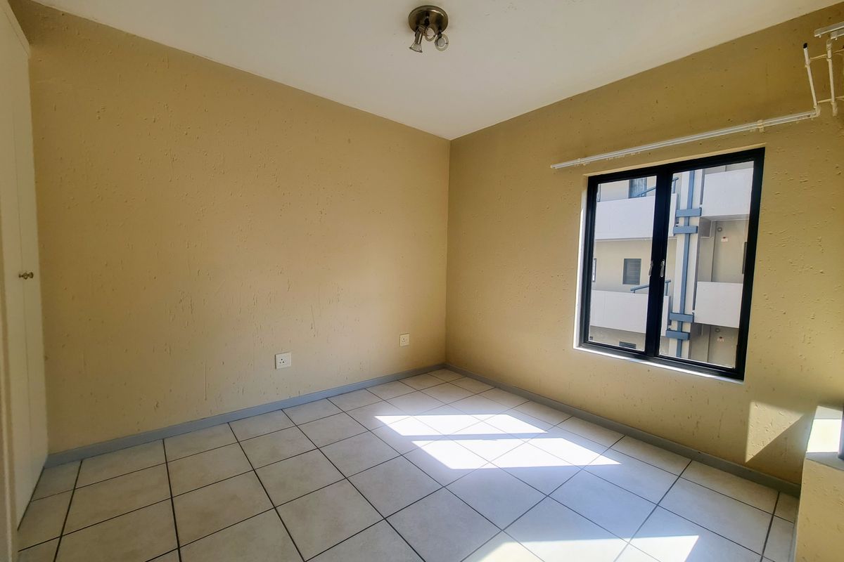 An empty bedroom featuring tiled flooring, a built-in cupboard, and an aluminium window frame, offering a blank canvas for personalization.