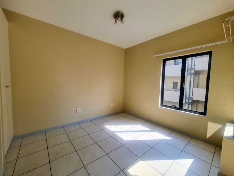 An empty bedroom featuring tiled flooring, a built-in cupboard, and an aluminium window frame, offering a blank canvas for personalization.