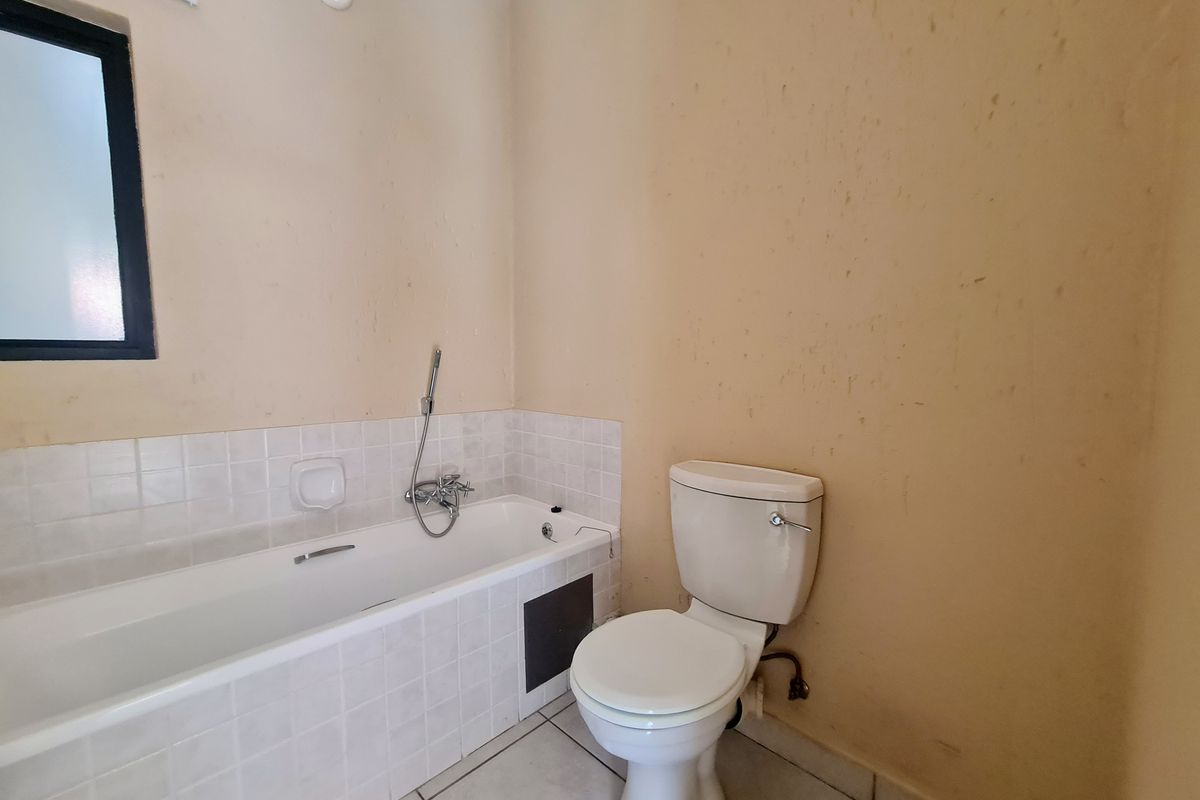 A functional bathroom featuring a bathtub with a handheld shower mixer, a standard toilet, and tiled finishes, currently requiring cosmetic updates to the wall surfaces.