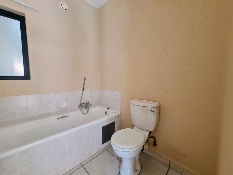 A functional bathroom featuring a bathtub with a handheld shower mixer, a standard toilet, and tiled finishes, currently requiring cosmetic updates to the wall surfaces.