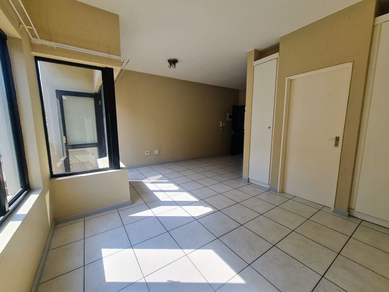 A spacious, empty bedroom featuring neutral tiled flooring, built-in cupboards, and an internal window providing natural light.